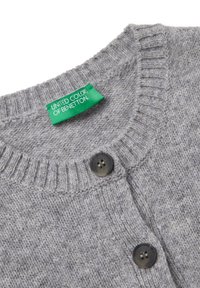 Šedý pletený cardigan s žebrovaným límcem, dvěma tmavými knoflíky a zelenou nášivkou "United Colors of Benetton" na límci.