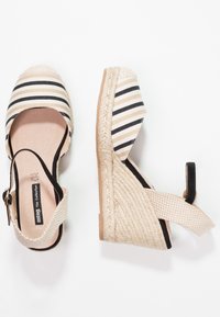 Espadrillas a zeppa con tomaia in tela a righe beige e nera, dotate di tacco avvolto in juta, cinturino alla caviglia regolabile e soletta imbottita.