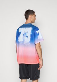 Maillot de sport en mesh avec un design dégradé, passant du bleu au rose. Présente un grand chiffre blanc "73" et des manches courtes.