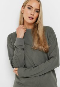 Sudadera de manga larga en verde oliva con puños acanalados y cuello redondo. Textura suave y corte holgado sin patrones visibles ni adornos.