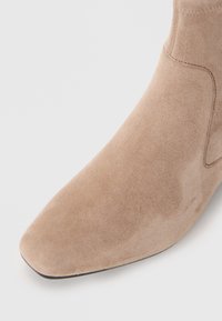 Beige suède enkellaars met een spitse neus, gladde textuur en minimale stikseldetails. Heeft een naadloos, gestroomlijnd ontwerp.