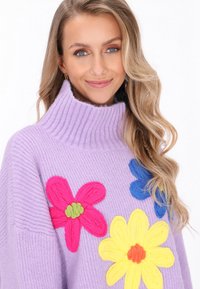 Liliowa dzianinowa sweter z wysokim kołnierzem, z żywą haftowaną florystyką w odcieniach różu, niebieskiego, żółtego i zielonego. Teksturowany i kolorowy design.