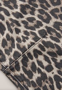 Tela vaquera con estampado de leopardo sobre un fondo beige, con manchas negras y marrones. La textura es suave con detalles de costura visibles.