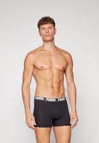 Schwarze Boxer-Shorts mit einem Logo-Bund. Weicher Stoff, enganliegende Passform und glatte Textur. Das Modell steht vor einem neutralen Hintergrund.