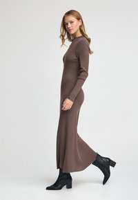 Brun ribbet strikket kjole med høj halsudskæring og lange ærmer, der går til ankel længde. Parret med sorte ankelstøvler med lynlås.