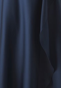 Tissu bleu marine avec une texture lisse et un design qui coule doucement, comportant un détail de bord incurvé le long d'un côté.