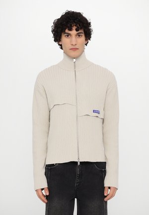 Pulover zip-up bej deschis, cu design ribflat, guler înalt și croială scurtă. Prezintă un patch cu logo pe partea stângă.