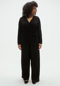 Juodas klostuotas kombinezonas su persipynimo dizainu, ilgomis rankovėmis, diržu juosmens srityje ir plataus kirpimo kelnėmis. Lygus paviršius su tekančia silueto linija.