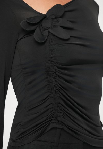 Fekete hosszú ujjú felső, virágos díszítéssel és redőzött textúrával a testen. Simított anyag, amely kiemeli a test vonalait.