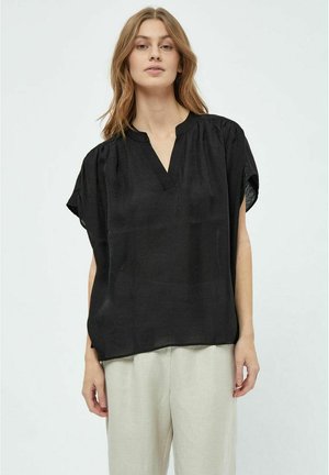 Zwarte blouse met korte mouwen en een V-hals, met geplooide schouders en een losse pasvorm, gecombineerd met lichte broeken. Glad textuur.