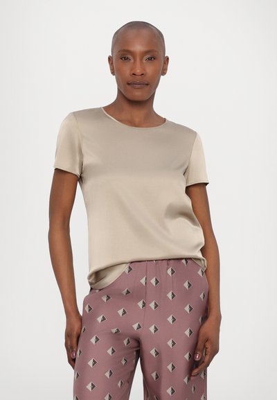 Top bege de manga curta em um tecido liso e brilhante com decote redondo, combinado com calças rosas estampadas com formas de diamante em cinza.