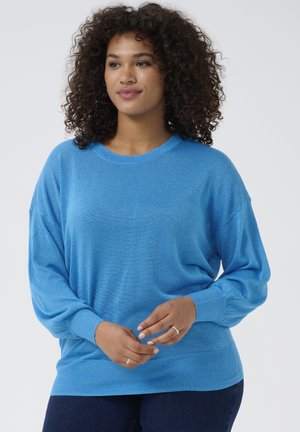 Blue knitted sweater featuring a round neckline, long sleeves, and a relaxed fit. Textured fabric adds visual interest. Paired with dark jeans.