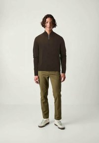 Pull encolure zippée brun foncé avec des manches longues, associé à un chino vert olive et des baskets blanches. Texture lisse, coupe décontractée.
