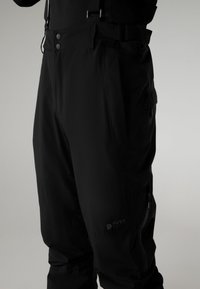 Pantaloni da sci neri impermeabili con bretelle regolabili, multiple tasche e cerniere, caratterizzati da una texture liscia e un design elegante.