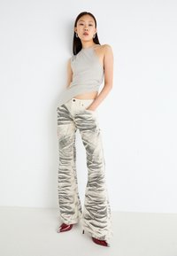 Beige halter top paired with high-waisted, flared pants featuring a graduated black marble pattern and deep pockets. Red pointed heels complete the look.