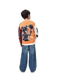 Barn som har på seg en fargerik genser med en tegneserie-tiger som spiller basketball, og vide, blå jeans, står vendt bort fra kamera.