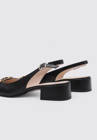 Zapatos negros de tipo slingback con punta redonda, tacón cuadrado bajo, material de cuero suave y acentos de estampado de leopardo en la parte superior.