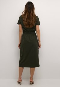 Olivgrön, kortärmad maxiklänning med elastisk midja som faller ner till halvkalv, tillverkad av mjukt bomullsmaterial med jämn yta.