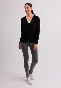 Svart kofta med v-ringad hals, knappframsidan och långa ärmar. Kombination med grå skinny jeans och vita sneakers för en avslappnad look.