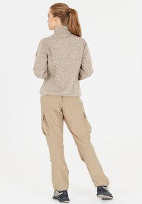 Fleece pullover in lichtbruin met hoge kraag, gecombineerd met beige cargobroek met zijzakken en een relaxte pasvorm.