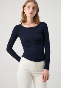 Navyblaues, geripptes Langarmshirt mit einem Rundhalsausschnitt, figurnahem Design und einem kleinen Logodetail; kombiniert mit hellen Jeans.