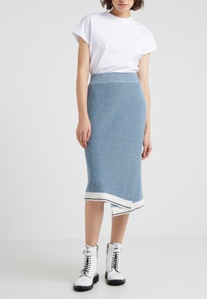 Falda de punto acanalado azul hasta la rodilla con acentos de dobladillo blanco, combinada con una camiseta blanca de manga corta y botas blancas de tobillo con cordones.