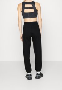 Top corto atlético negro con diseño de espalda cortada, combinado con pantalones jogger negros y zapatillas negras. Tejido suave con puños elásticos.
