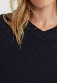 Pull en maille bleu marine avec un décolleté en V ; présente une texture côtelée au niveau du col et de l'ourlet ; tissu doux de poids moyen.