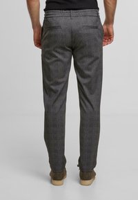 Gray check patterned trousers with a tapered fit, made of fabric with a smooth texture, featuring two back pockets and a waistband detail.