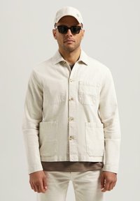 Lys beige jakke laget av teksturert stoff, med krage, knappestolpe og to frontlommer. B�året med en brun topp og caps.