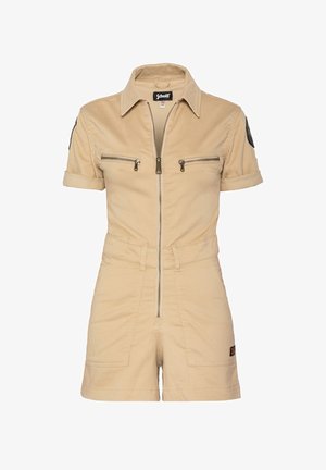 Combinaison en coton beige à manches courtes, avec fermeture éclair à l'avant, deux poches poitrine et taille cintrée. Présente un écusson noir sur la manche gauche.