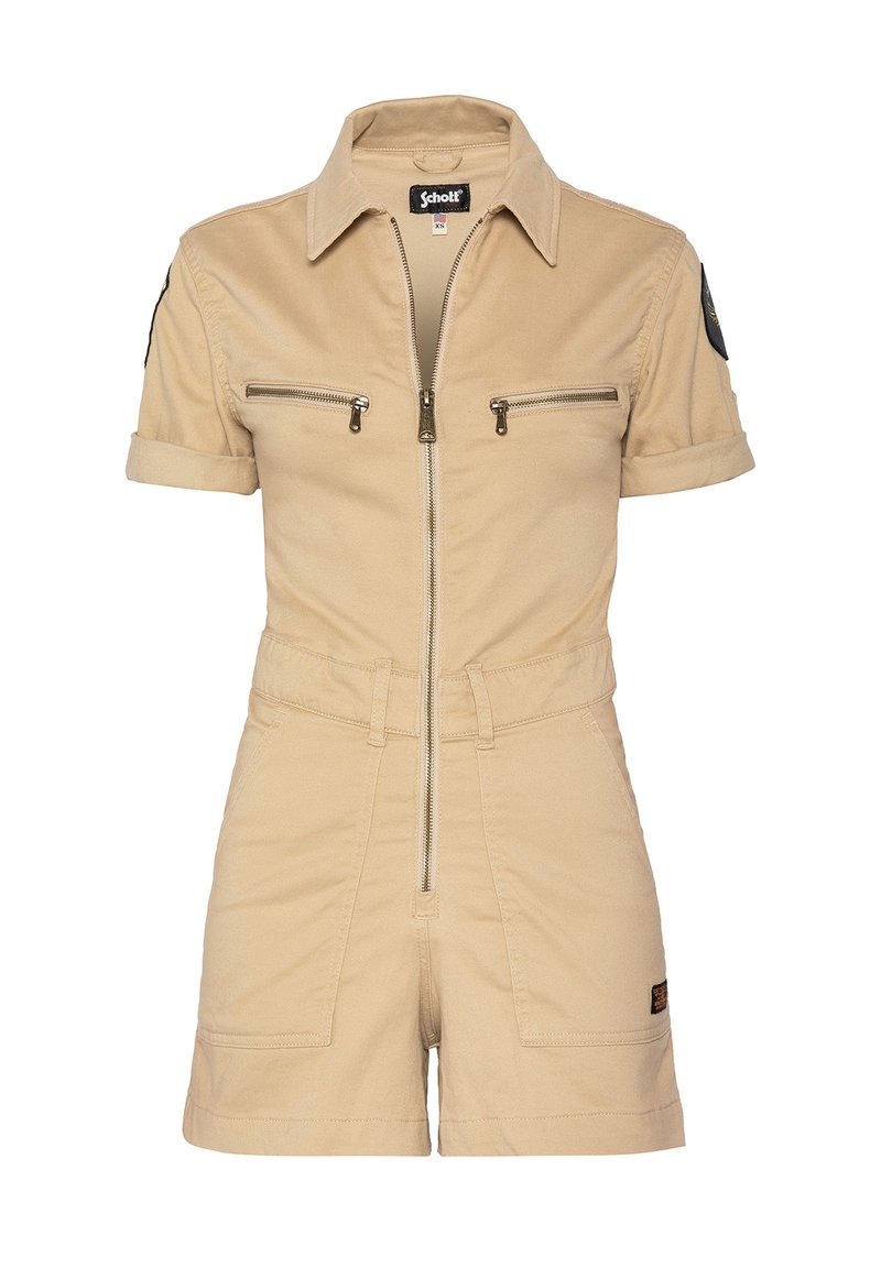 Tuta di cotone beige con maniche corte, chiusura frontale con zip, due tasche sul petto e vita aderente. Presenta una toppa nera sulla manica sinistra.