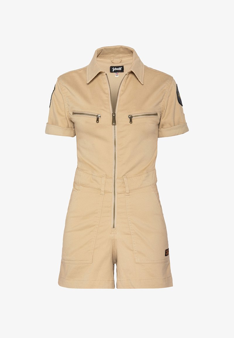 Tuta di cotone beige con maniche corte, chiusura frontale con zip, due tasche sul petto e vita aderente. Presenta una toppa nera sulla manica sinistra.