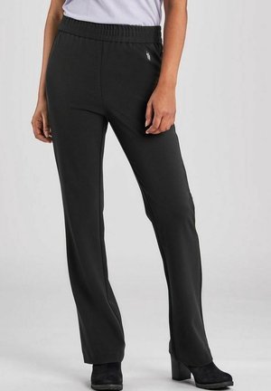 Femme portant un pantalon noir à jambes droites avec une taille élastique et un petit logo brodé, associé à des bottines noires à talons.