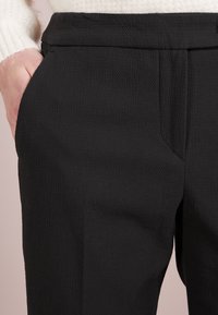 Svarta texturerade byxor har en skräddarsydd passform med sidofickor och en mjuk midja, vilket framhäver en sofistikerad design.