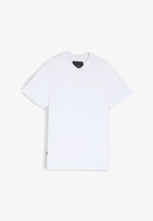 Biała koszulka polo z bawełny, z klasycznym kołnierzykiem, zapięciem na trzy guziki i krótkimi rękawami. Posiada subtelny detal z logo na klatce piersiowej.