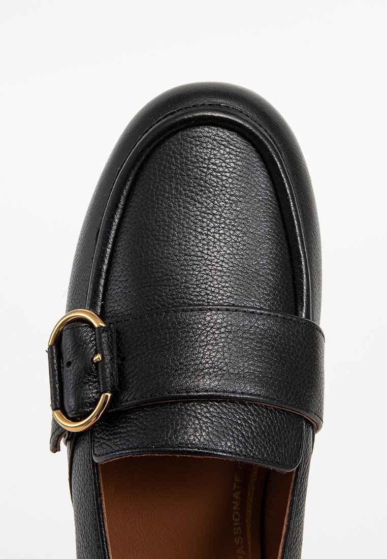 Czarne skórzane loafersy o teksturowanym wykończeniu z złotą klamrą z boku, ukazujące górną część i częściowe wnętrze brązowej wkładki.