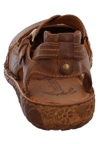 Brown leather sandal featuring multiple straps, brass hardware, textured sole with floral details, and an open-back design for breathability.