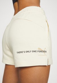 Lichtbeige shorts met een elastische tailleband, zijzakken en een bedrukte slogan "ER IS MAAR ÉÉN FOREVER" in zwart, met een gouden logo-accent.