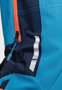 Niebieska i granatowa tkanina z pomarańczowym zamkiem błyskawicznym. Posiada odblaskowy detal oraz smukły design z kontrastowymi przeszyciami.