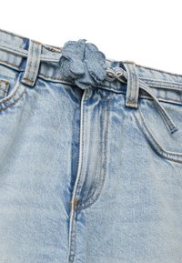 Světle modré džíny z denimu se staženým pasem, se slabým květinovým látkovým akcentem a viditelným šitím a kapsami.