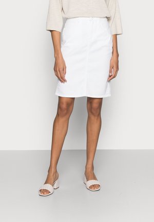 Femme portant une jupe blanche mi-longue, un haut beige à manches trois-quarts et des sandales beiges à talon bloc ouvert au niveau des orteils.