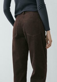 Pantalon en velours côtelé marron avec une surface texturée, doté de deux poches arrière et d'une taille haute, associé à un haut gris ajusté.