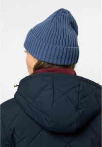Strikket blå lue med ripete tekstur og spiss topp, brukt sammen med en marine blå quiltet jakke med maroon krage.