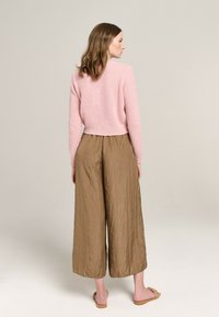 Helles rosa, kurzes Sweatshirt mit strukturiertem Finish, kombiniert mit braunen, locker sitzenden, knautschigen weiten Hosen und flachen Sandalen.