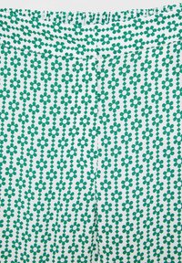 Grön och vit mönstrad tyg med små blommönster och diamantformer. Slät textur, elastisk midja och plana sömmar.