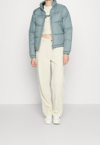 Light blue puffer jacket with high collar, front zipper, and elastic cuffs, paired with cream-colored wide-leg pants and white sneakers.