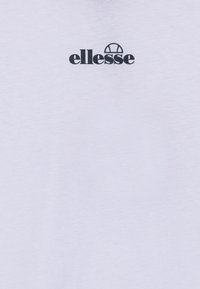 Hvit bomull t-skjorte med svart "ellesse"-logo og et sirkulært designelement over teksten. Glatt tekstur, korte ermer, vanlig passform.