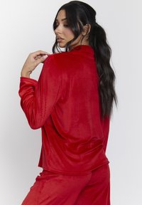 Rode geribde loungewear set bestaande uit een top met lange mouwen en broek. De stof heeft een zachte textuur met een relaxte pasvorm en afgezakte schouders.