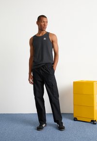 Zwarte cargobroek met zijzakken, gecombineerd met een donkergroen tanktop met een klein wit logo. Zwarte sneakers maken de outfit compleet.